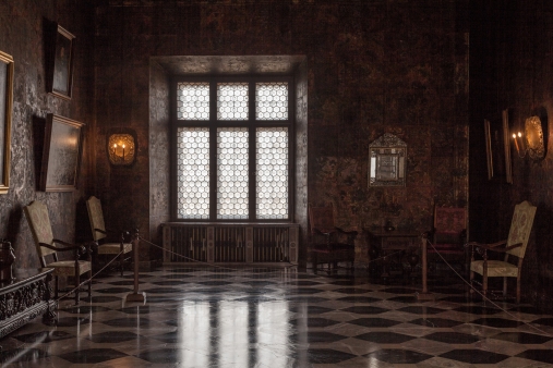 komnata zamku, półmroczna, częściowo oświetlona światłem z dużego okna, na ścianach obrazy i  świeczniki, marmurowa podłoga, kilka krzeseł pokrytych tkaniną