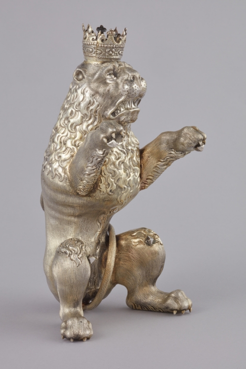 wykonana ze srebra złoconego figurka lwa z koroną na głowie, stojącego na dwóch łapach