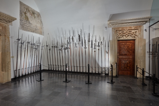 otwarta przestrzeń z prezentowaną bronią drzewcową. odsłonięty fragment średniowiecznego malowidła w lewym górnym rogu