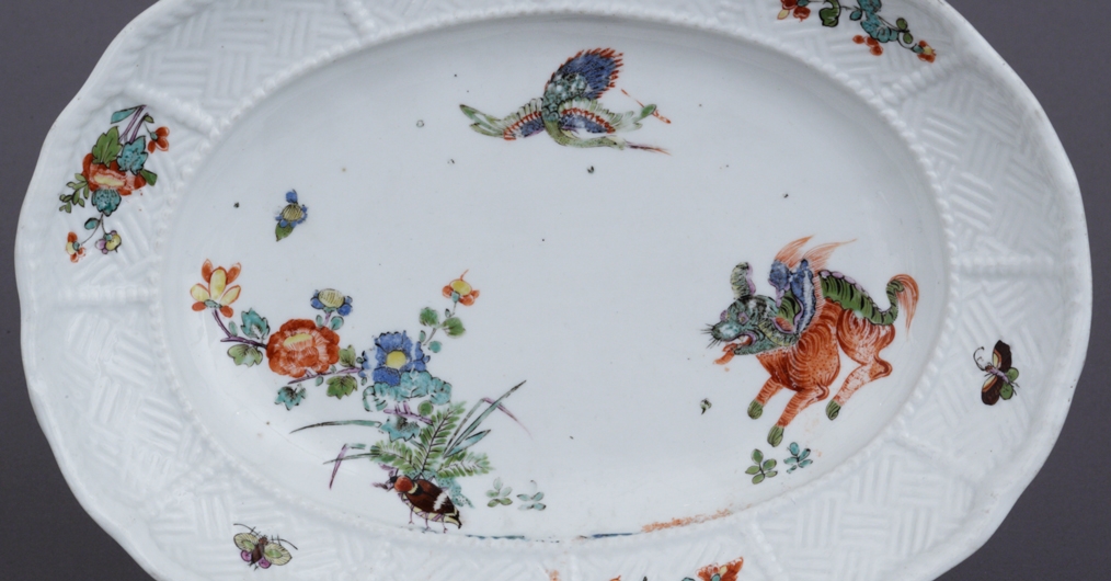 Na zdjęciu widoczny jest owalny talerz - patera. Wykonany jest z białej ceramiki i ozdobiony kolorowymi motywami kwiatowymi oraz fantazyjnymi przedstawieniami zwierząt.