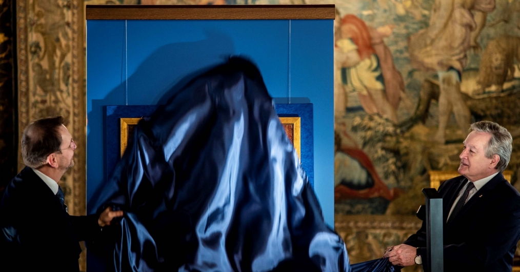 w zabytkowej sali zamku dwóch mężczyzn zdjemuje niebieską załonę z obrazu zawieszonego na ścianie