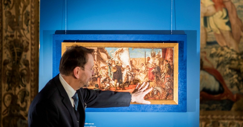 mężczyzna wskazuje ręką na obraz, przedstawiający scenę hołdu pruskiego