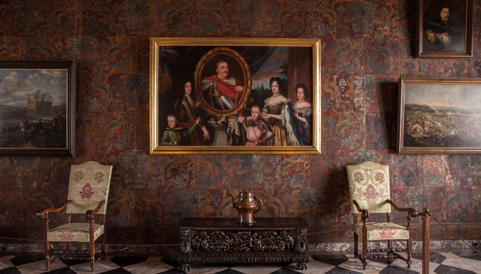 zabytkowa komnata zamku, ściany pokryte kurdybanem, duży obraz - portret rodziny królewskiej, obok dwa zabytkowe krzesła