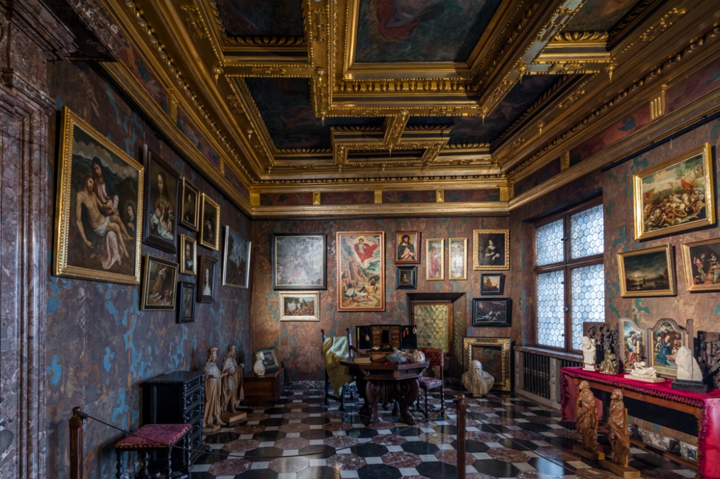niewielka sal aw zamku, naścianach tkaniny i obrazy, na stołacj ustawione drobne przedmnioty rzemiosła artystycznego i kolekcjonerskie