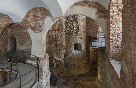 Zdjęcie przedstawia stare wnętrze zamku o łukowych sklepieniach. Ściany są ceglane i częściowo pokryte białym tynkiem.