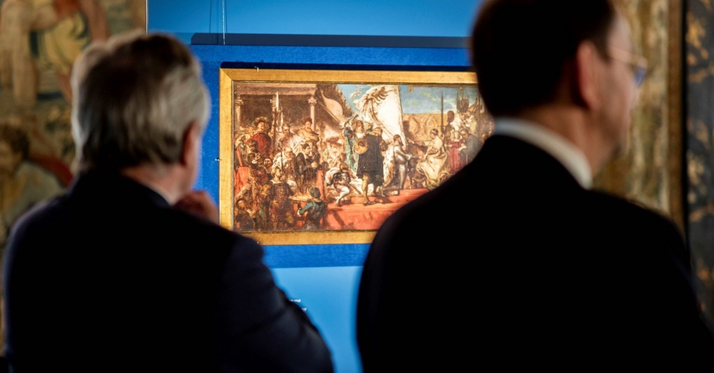 sylwetki dwóch mężczyzn, widziane od tyłu, w tle obraz pradstawiający scenę hołdu pruskiego