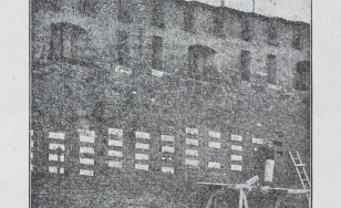 stare zdjęcie przedstawiające ceglany mur, z wmontowanymi cegiełkami z kamienia, na rusztowaniu rzemieślnik pracujący przy wstawianiu cegiełek