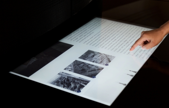 Ekran dotykowy z fragmentem tekstów i zdjęciami, z prawej strony ręka z palcem dotykającym ekran