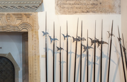 Zdjęcie przedstawia zawieszoną na ścianie zbrojowni ozdobną broń. Fragment ekspozycji znajduje się na tle białej ściany, obok ozdobny portal z piaskowca.