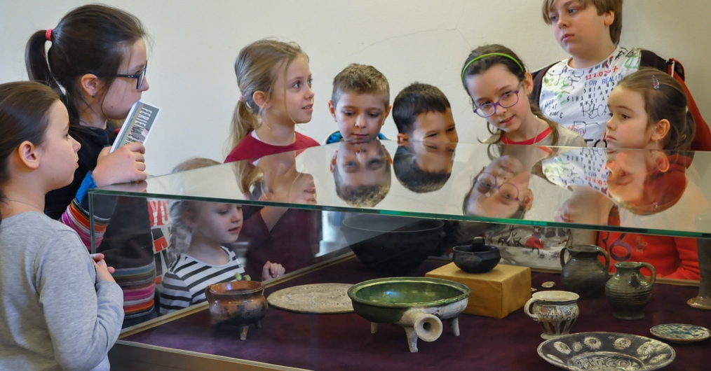 grupa dzieci przyglądająca się obiektom zabytkowym ułożonym w gablocie