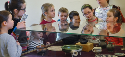 grupa dzieci przyglądająca się obiektom zabytkowym ułożonym w gablocie