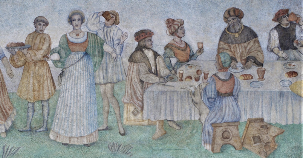 fragment malowidła ściennego, scena uczty, uczestnicy w średniowiecznych strojach tańczą, siedzą za stołem, na którym rozłożone są naczynia i potrawy
