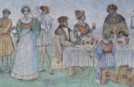 fragment malowidła ściennego, scena uczty, uczestnicy w średniowiecznych strojach tańczą, siedzą za stołem, na którym rozłożone są naczynia i potrawy