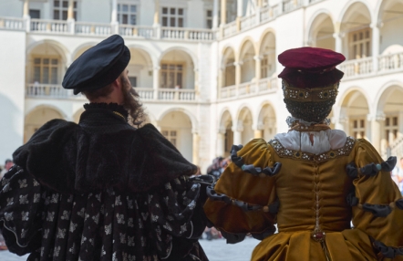 kobieta i mężczyzna w renesansowych strojach, stoją tyłem do widza, na tle dziedzińca zamkowego