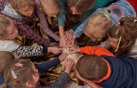 Grupa dzieci w wieku szkolnym siedzi na podłodze, tworząc krąg nad tkaniną
