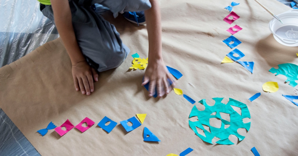 dziecko opiera się ręką o materiał, na którym położone są ornamenty wycięte z papieru