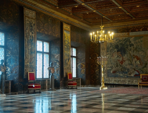 sala w zamku, rozświetlona nastrojowym światłem wpadającym przez okna, na ścianach arrasy - zabytkowe tkaniny