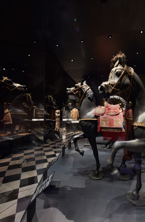 wnętrze wystawy z obiektami wawelskiego skarbca koronnego, w gablotach rozmieszczone zabytki, na modelach koni umieszczone elementy osiodłania i uprzęży