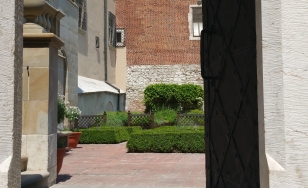 Widok przez bramę do ogrodu wawelskiego, w tle rabaty z roślinami i mury zamku