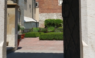 Widok przez bramę do ogrodu wawelskiego, w tle rabaty z roślinami i mury zamku