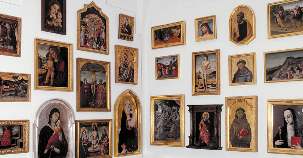 Zdjęcie przedstawia powieszone na białej ścianie obrazy o tematyce religijnej, oprawione w złote ramy.