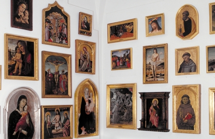 Zdjęcie przedstawia powieszone na białej ścianie obrazy o tematyce religijnej, oprawione w złote ramy.