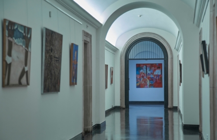 oświetlony korytarz w starym budynku, na ścianach zabytkowe obrazy