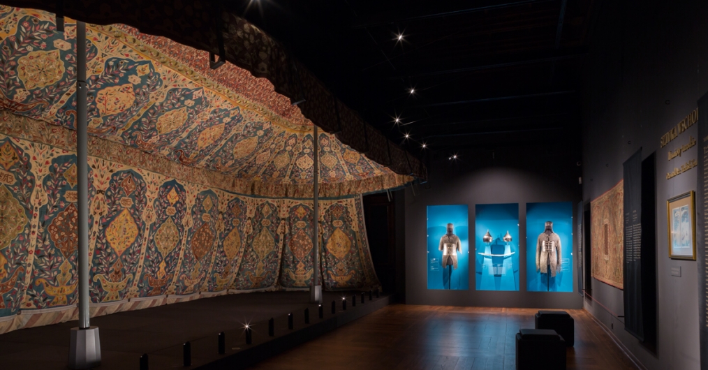 sala wystawy z namiotami tureckimi, w nastrojowo oświetlonym wnętrzu rozmieszczone obiekty muzealne: namioty, broń, elementy uzbrojenia