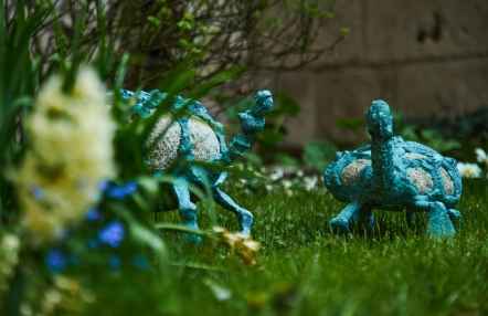 ogród, a w nim ustawione dwie stylizowane rzeźby żółwi, kamień połączony z metalem w kolorze zielonym