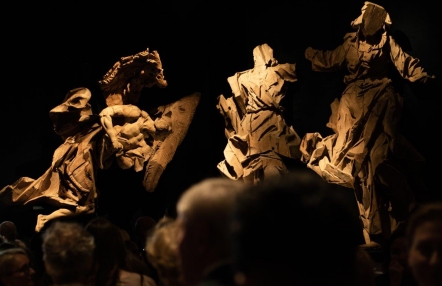 z półmroku wyłaniają się ogromne drewniane rzeźby, przedstawiające postacie w rozwianych szatacg