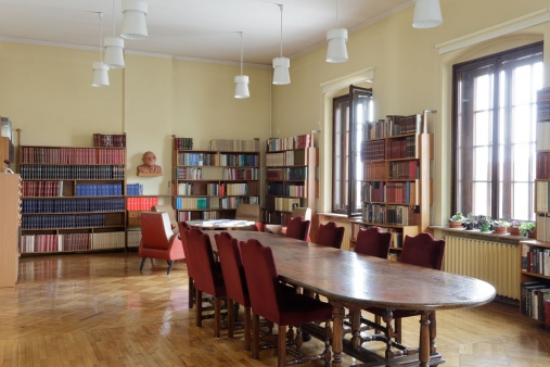 Współczesne wnętrze biblioteki z podłużnym stołem na środku pomieszczenia z zaokrąglonymi narożnikami.