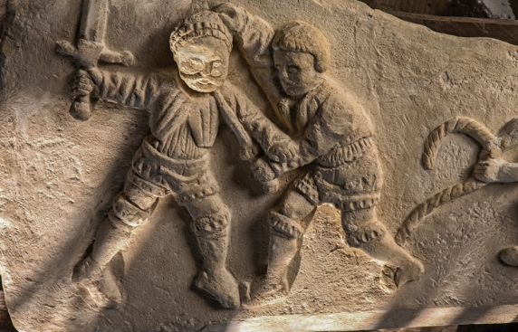 Fragment kaminnej płaskorzeźby przedstawiającej dwie walczące ze sobą męskie postacie