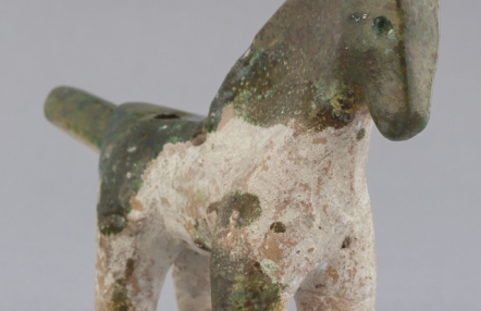 Zdjęcie przedstawia starą glinianą zabawkę w kształcie konia. Figurka jest niewielkich rozmiarów, a glina, z której została wykonana jest dwukolorowa.
