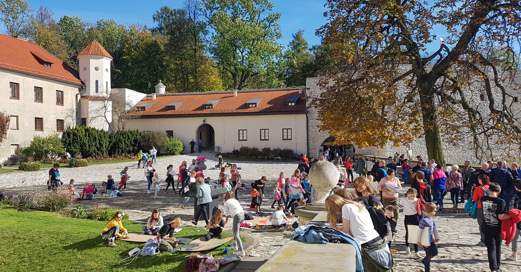 Zdjęcie przedstawia uczestników wydarzenia, głównie uczniów szkoły, malujących w scenerii zamkowej.