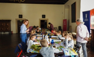 Zdjęcie przedstawia uczestników wydarzenia podczas tworzenia prac plastycznych w jednej z sal zamku.