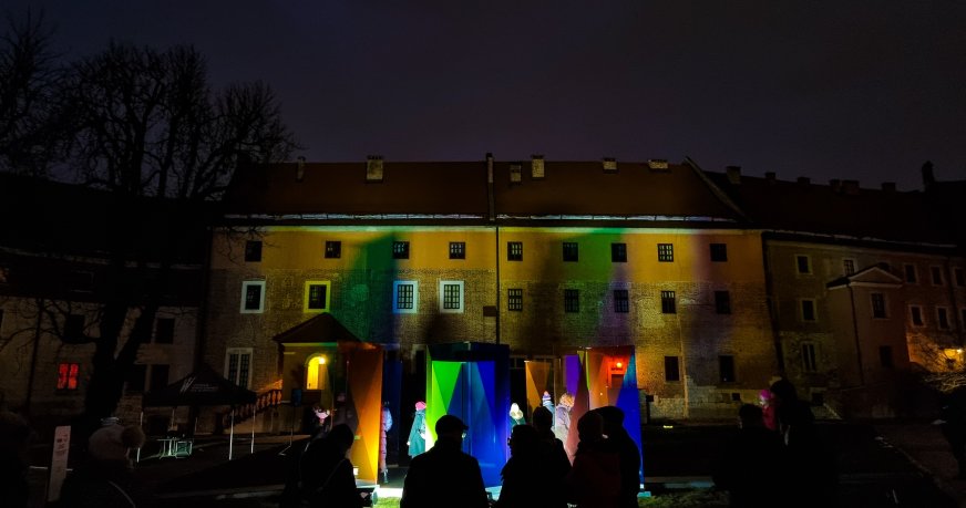 Podświetlona instalacja z kolorowych szkieł na tle wawelskiego budynku.
