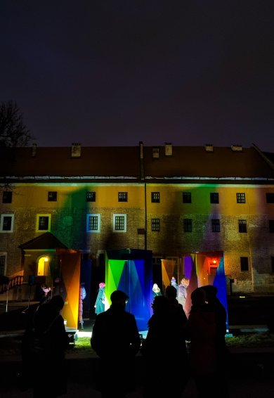 Podświetlona instalacja z kolorowych szkieł na tle wawelskiego budynku.