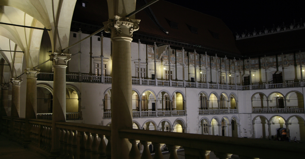 Nocny widok dziedzińca z licznymi oknami, które migoczą w ciemności, nadając miejscu wyjątkowy urok.
