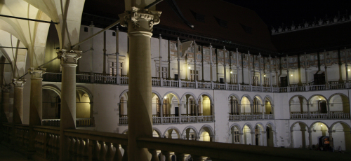 Nocny widok dziedzińca z licznymi oknami, które migoczą w ciemności, nadając miejscu wyjątkowy urok.