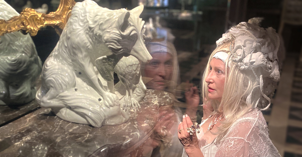 kobieta w fantazyjnym białym nakryciu głowy klęczy przed porcelanową figurką lisa