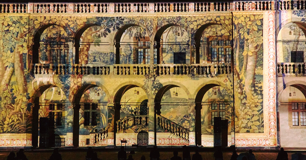 nocny widok krużganków dziedzińca arkadowego, na ich tle wyświetlane powiększone zdjęcia arrasów