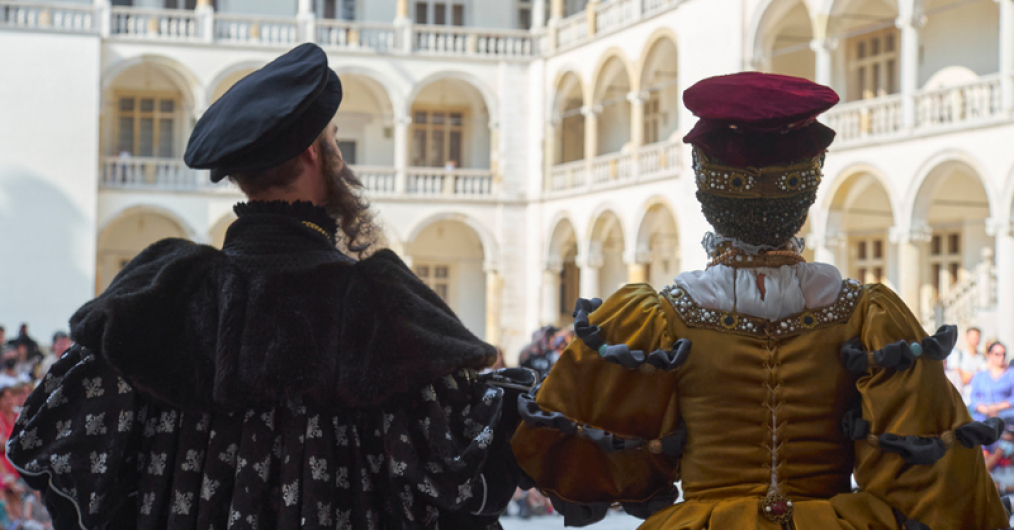 kobieta i mężczyzna w renesansowych strojach, stoją tyłem do widza, na tle dziedzińca zamkowego