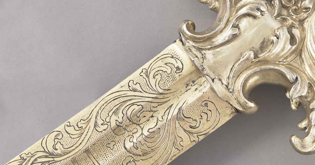 fragment miecza, w złotym kolorze, zdobionego rytym ornamentem roślinnym