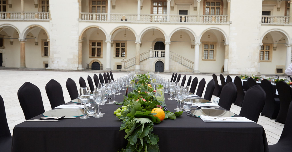 zastawiony naczyniami stół jadalny, w tle krużganki wawelskiego dziedzińca