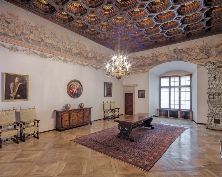 Sala w zamku z drewnianą podłogą, obrazami oraz freskami na ścianach