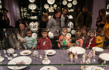 Grupa zwiedzających ogląda porcelanę w muzeum, z zainteresowaniem przyglądając się eksponatom.