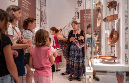 Grupa ludzi ogląda ekspozycję miedzianych garnków w muzeum