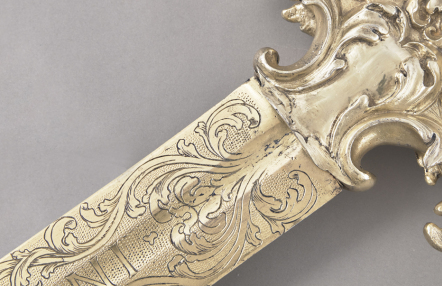 fragment miecza, w złotym kolorze, zdobionego rytym ornamentem roślinnym