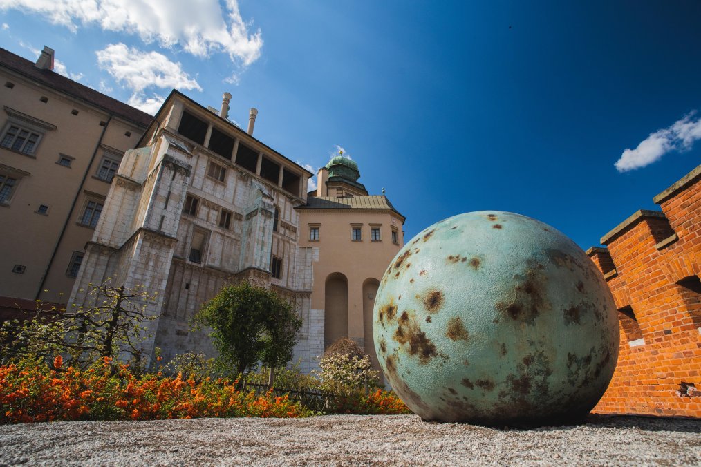 Duża kulista forma leży przed zamkiem, tworząc kontrast z jego architekturą.
