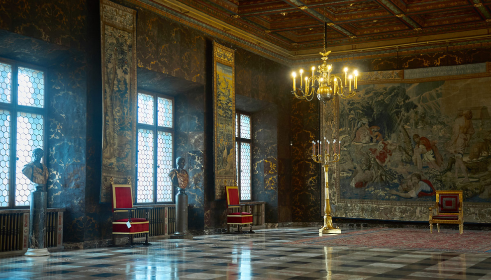 Przestronny sala zamku z dużą tkaniną na ścianie i kilkoma rzeźbami, które wzbogacają wystrój i nadają mu elegancji.